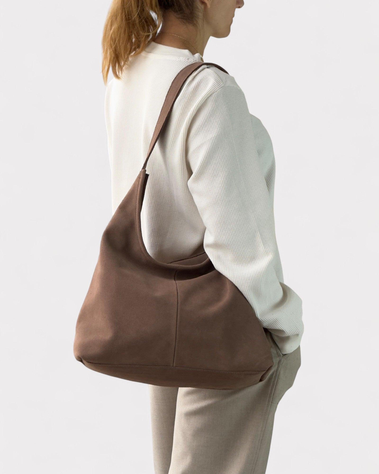 Person wearing a taupe shoulder bag on a plain background