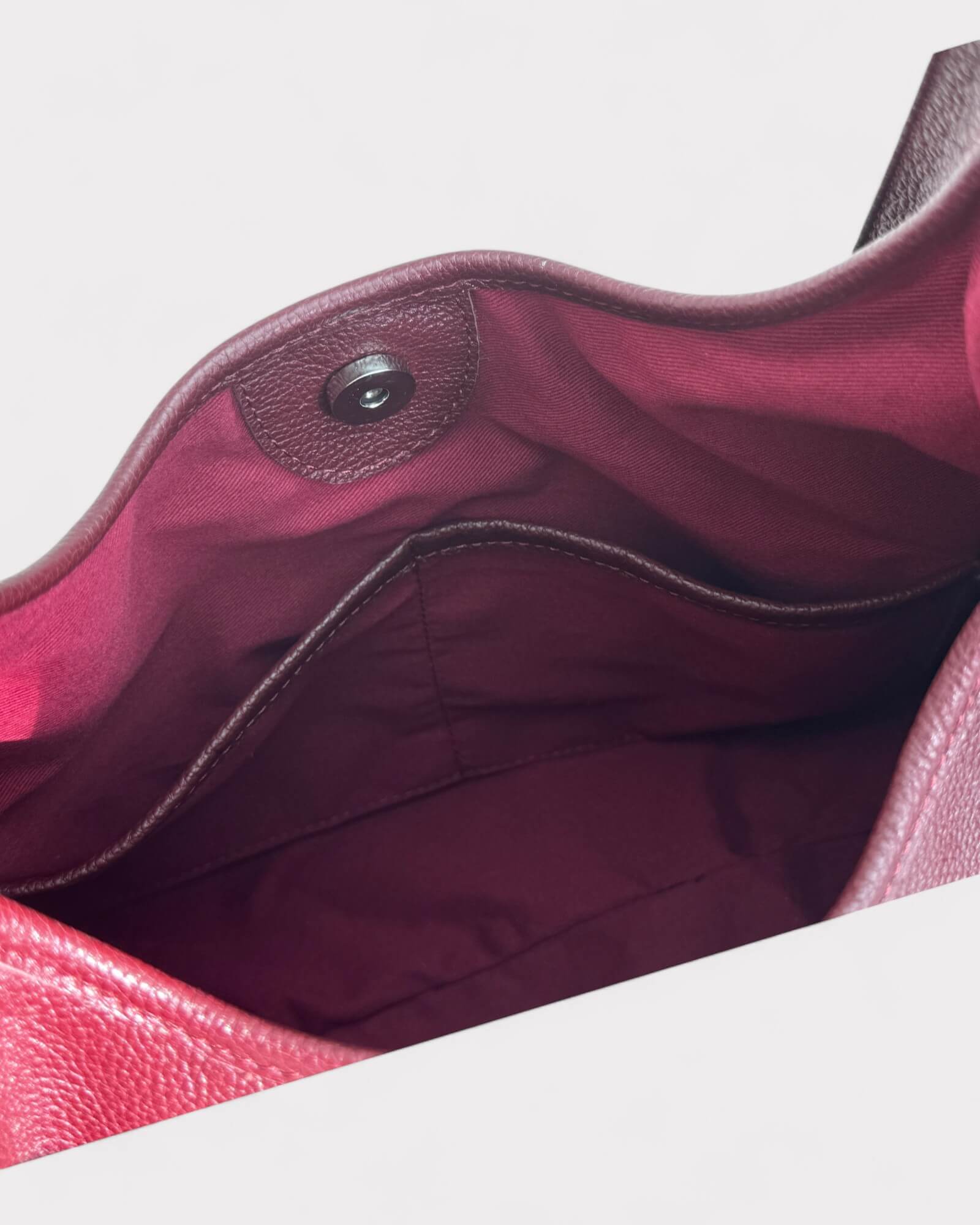 Close-up of a burgundy handbag with a magnetic snap on a light gray background