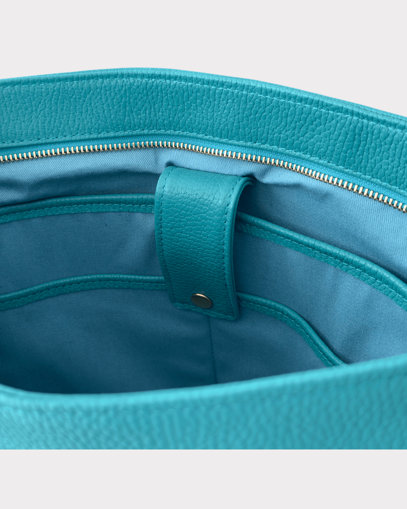 Close-up of a teal handbag with a gold zipper and strap and a laptop pocket