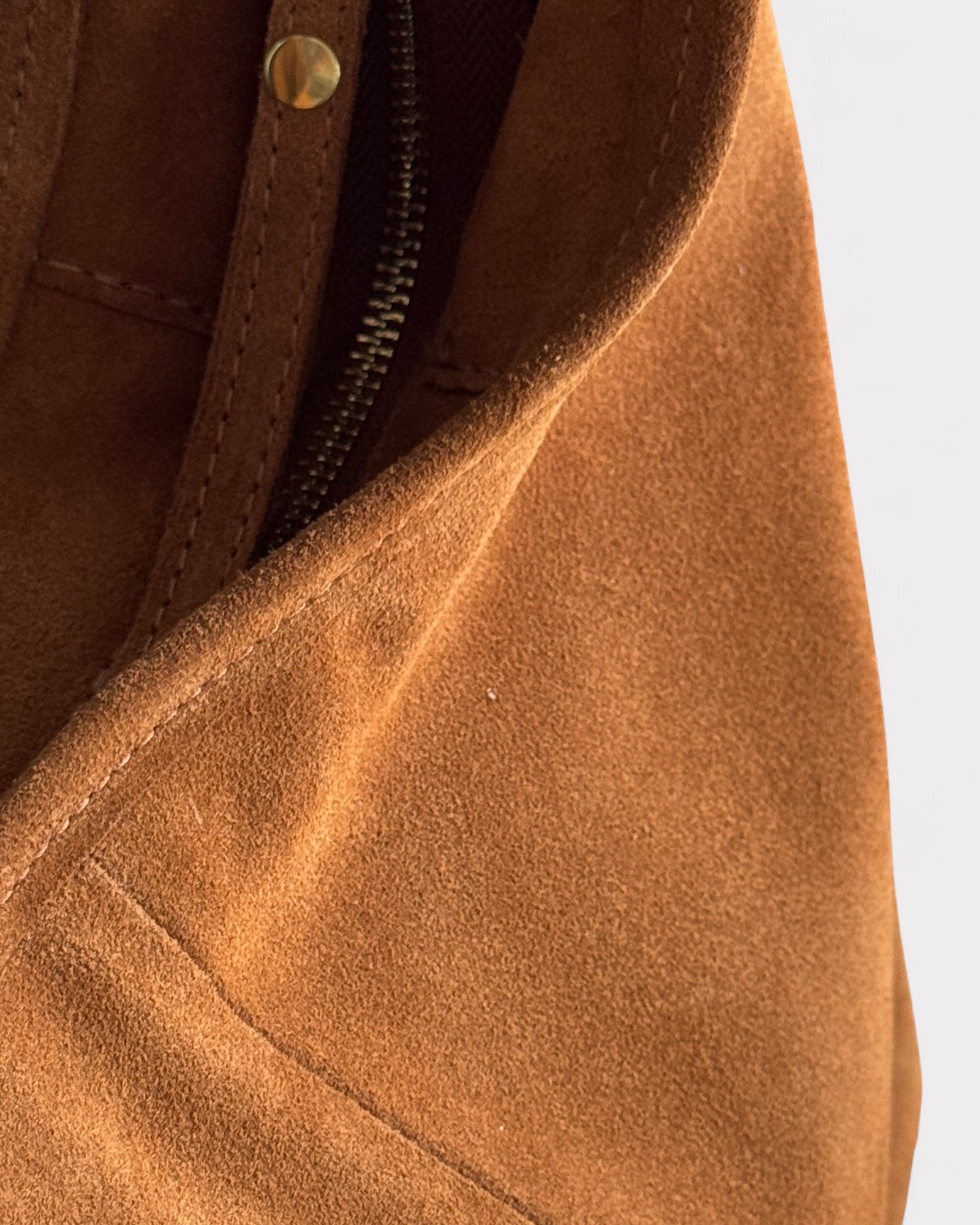 Close-up of a tan suede jacket with a zipper detail on a light gray background