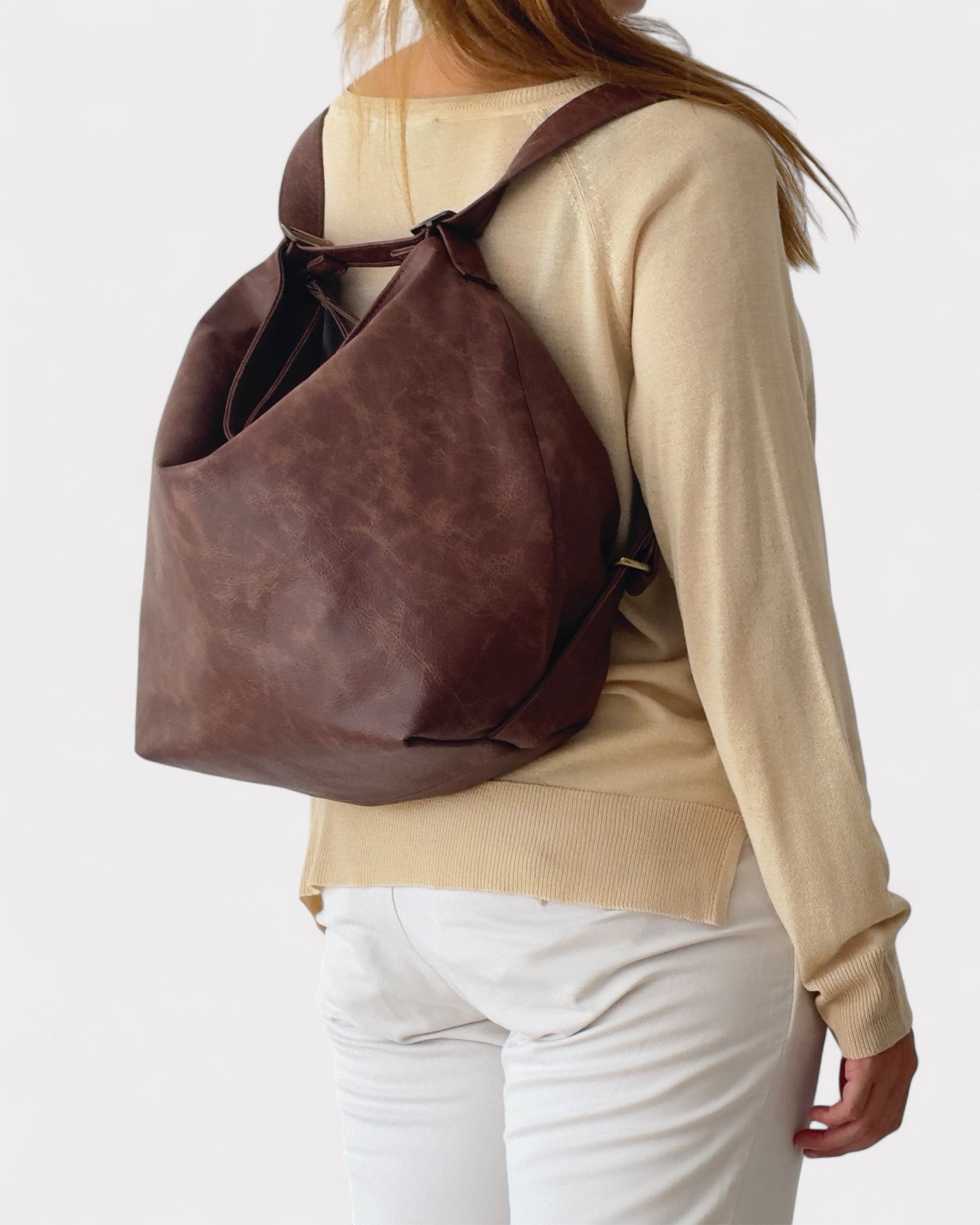 Person wearing a brown leather backpack on a plain background