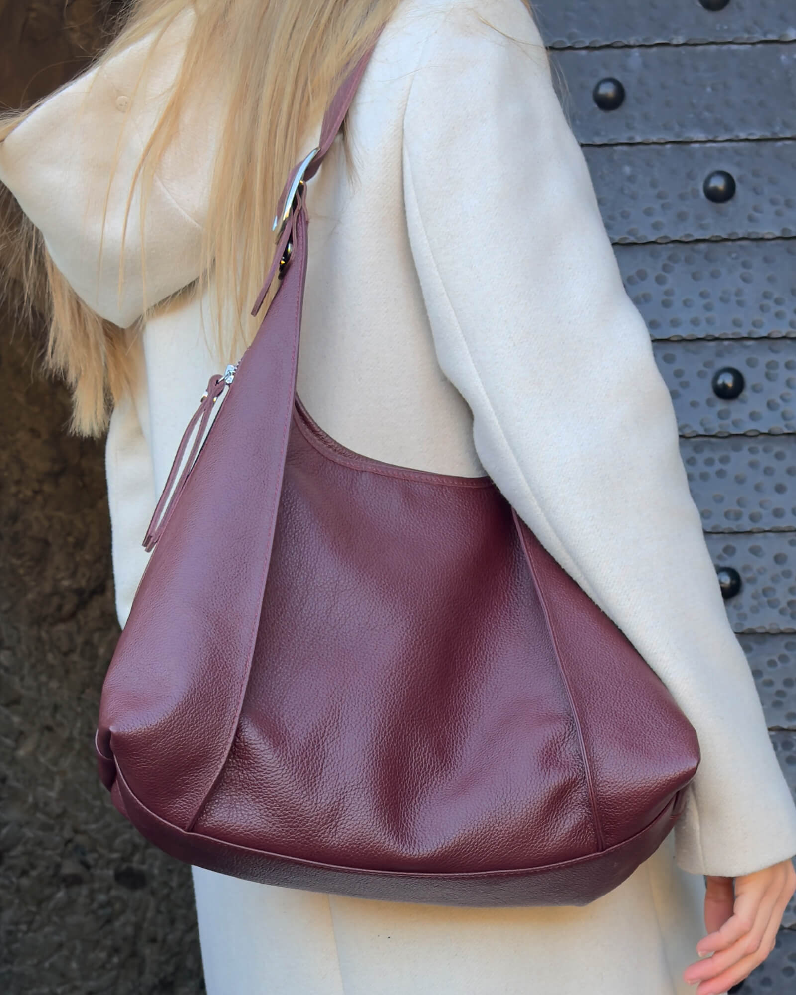 Person wearing a burgundy leather handbag against a textured wall background