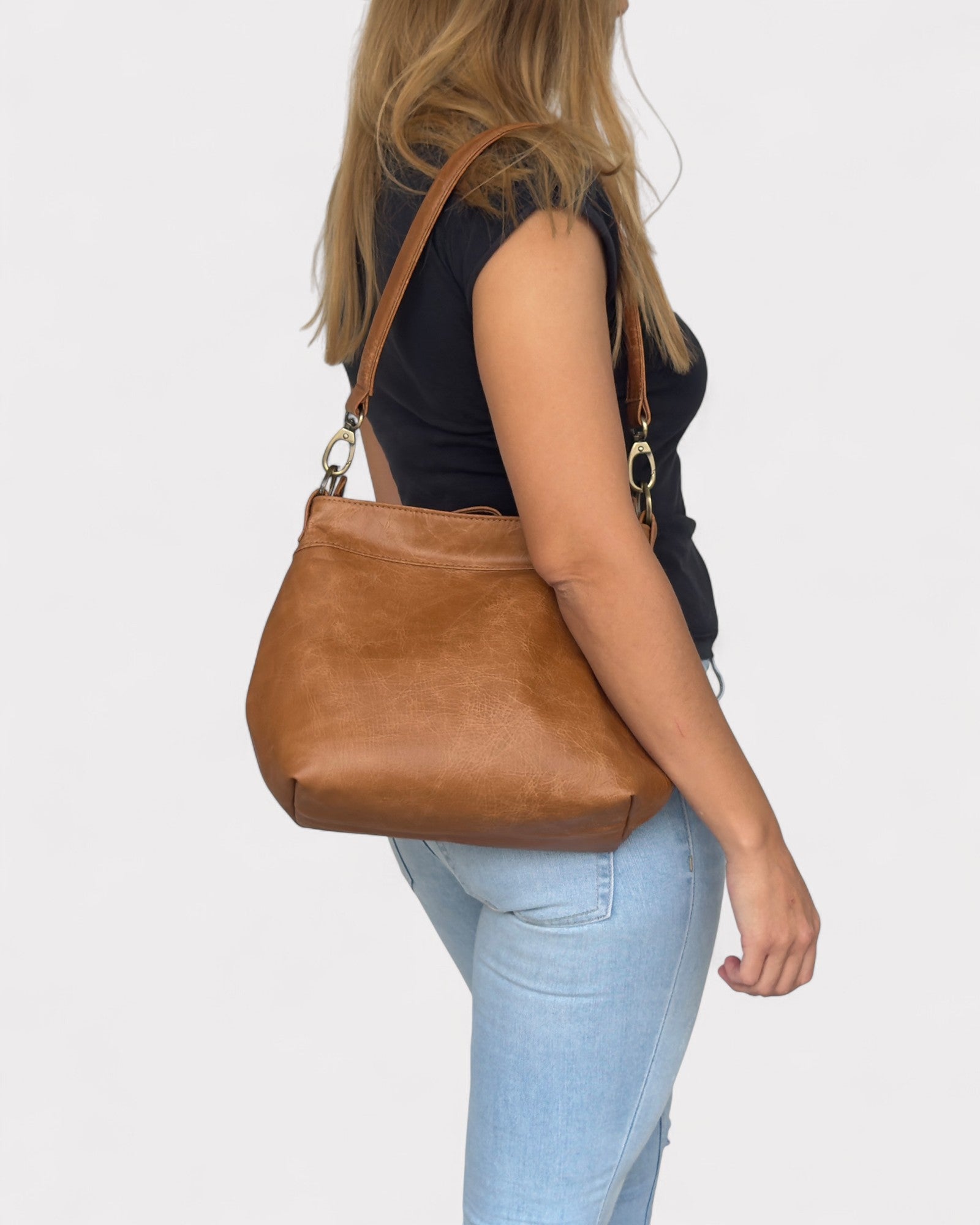 Person wearing a tan distressed shoulder bag on a plain background