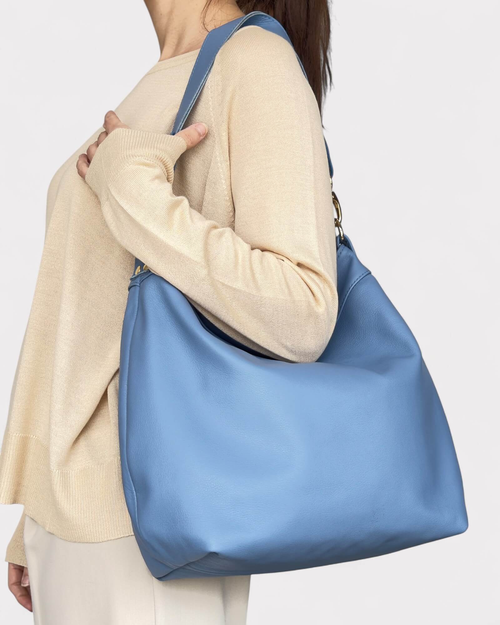 Person wearing a large blue shoulder bag on a plain background