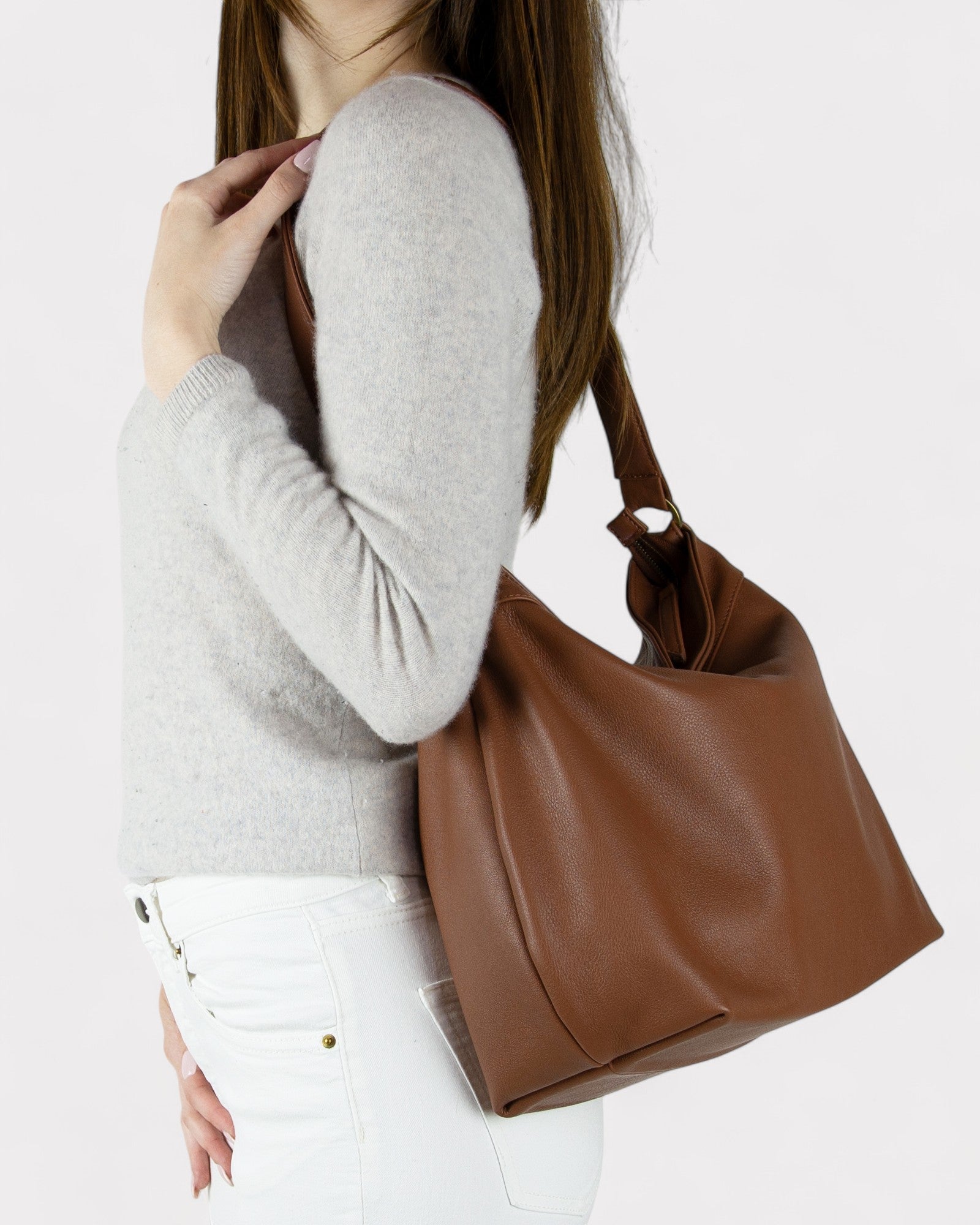 Person holding a cognac brown leather handbag against a white background
