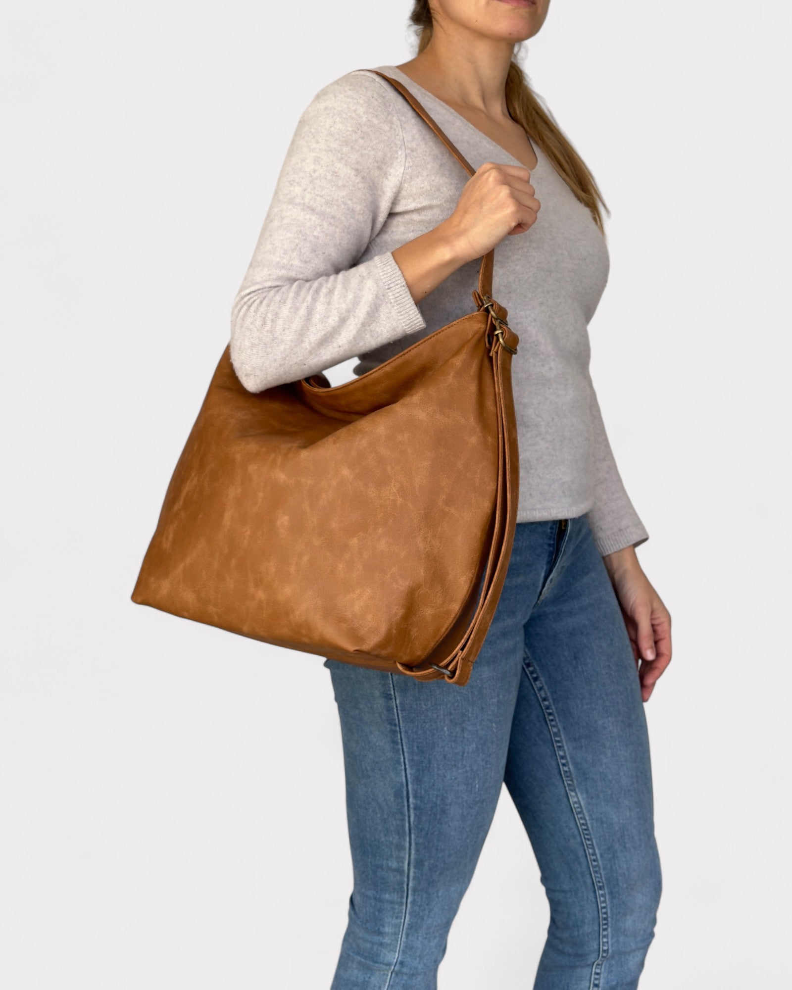 Woman holding a tan leather bag against a plain background