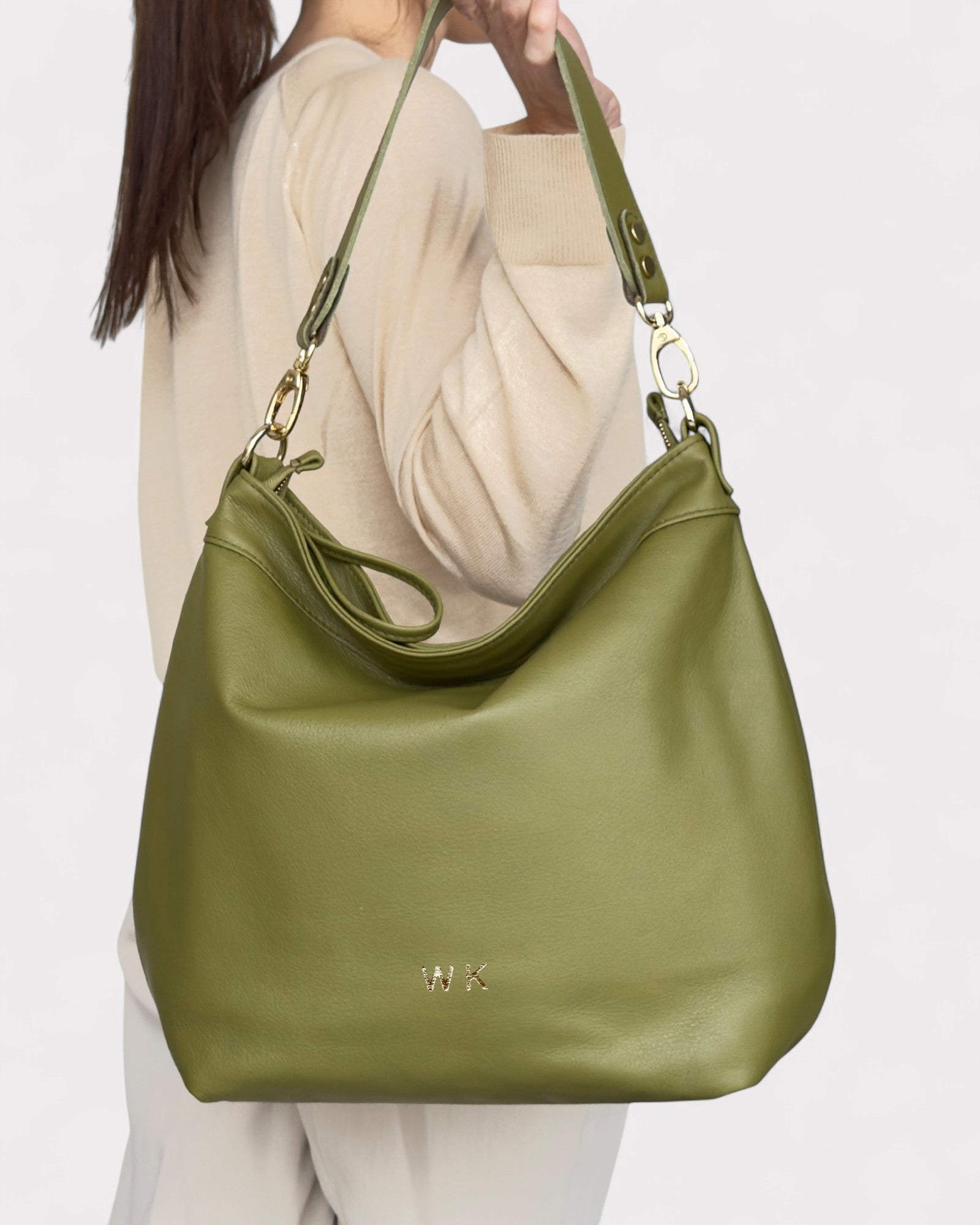 Green handbag with gold hardware held by a person against a white background