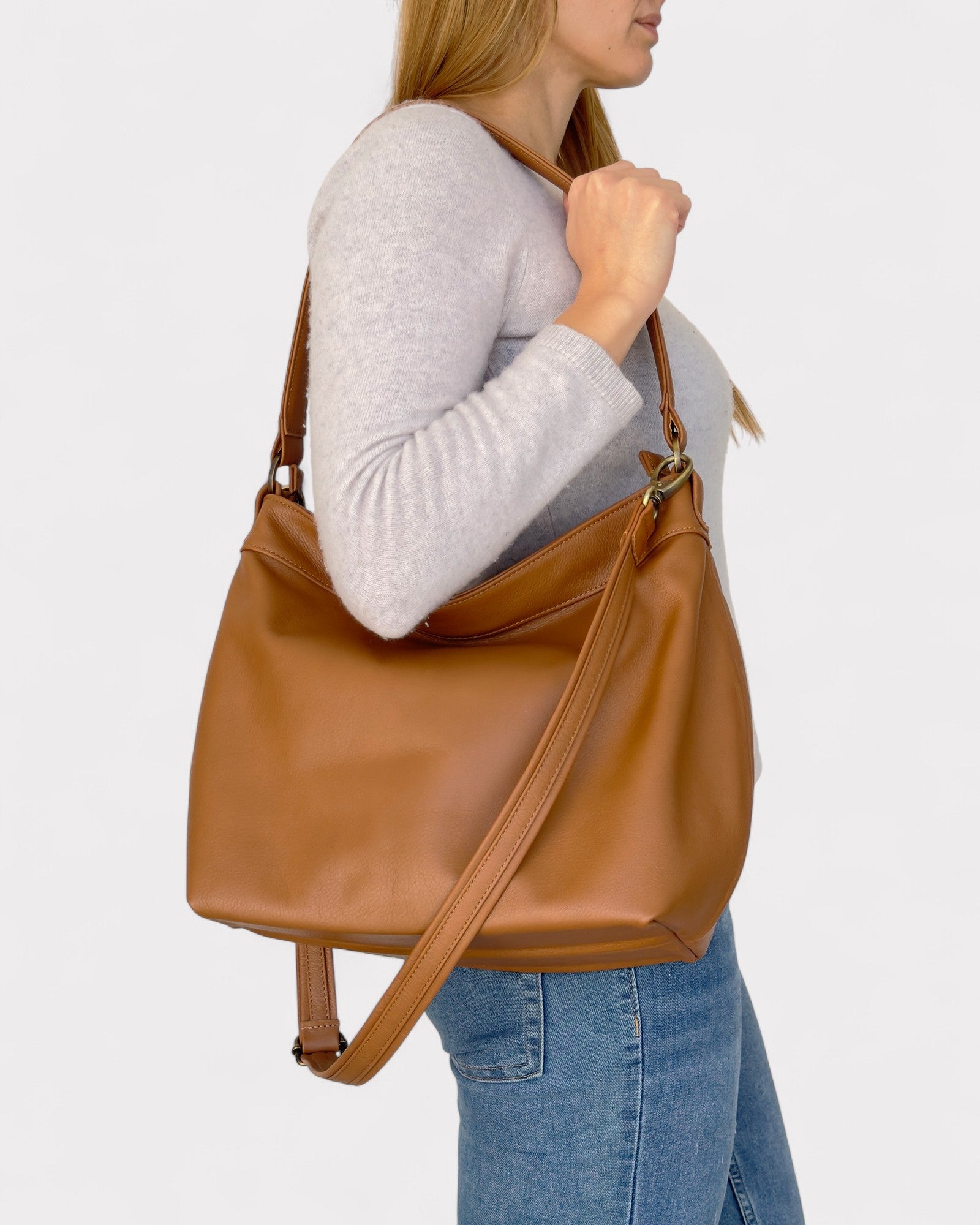 Person holding a tan leather bag against a plain background