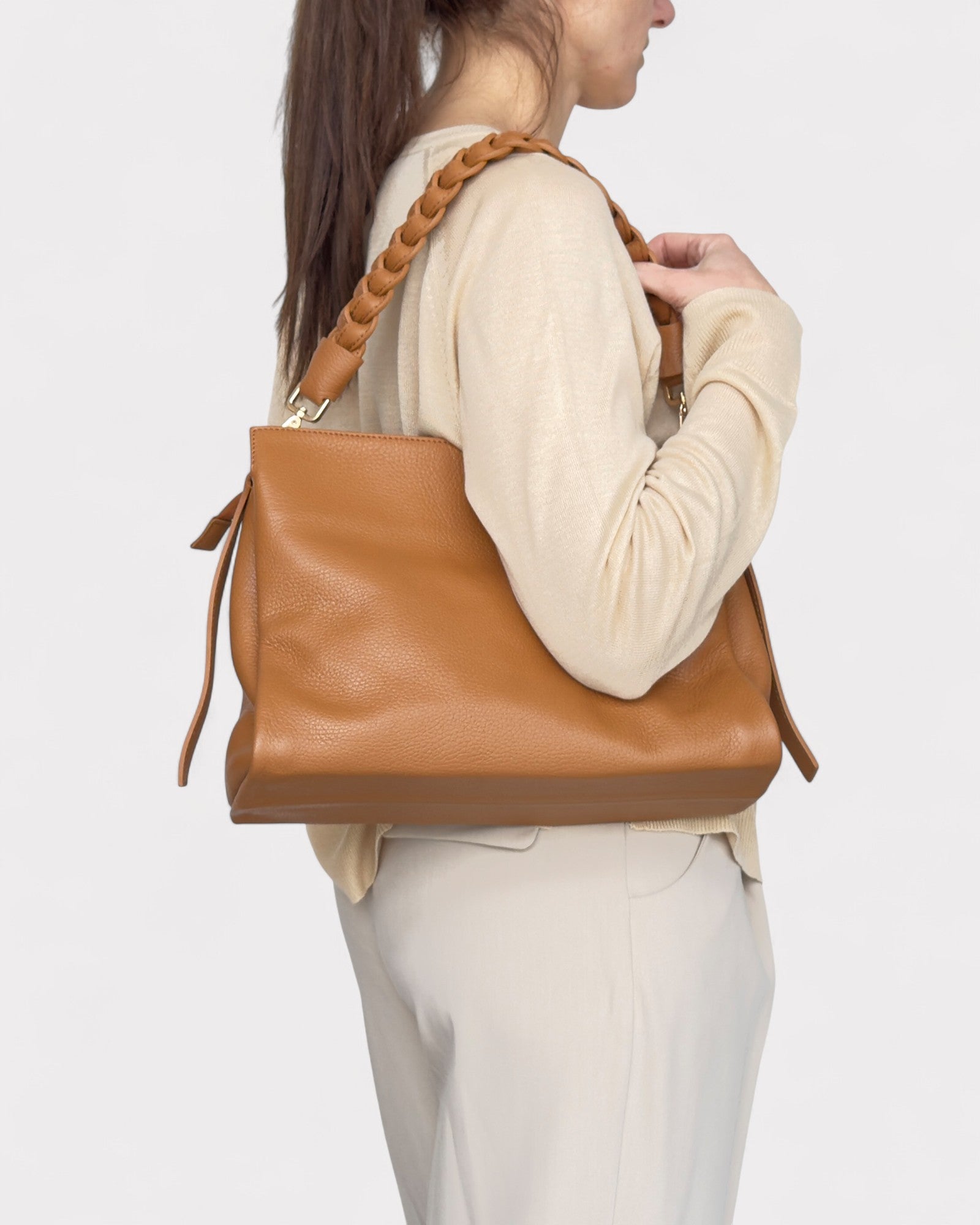 Person wearing a tan leather handbag on a plain background