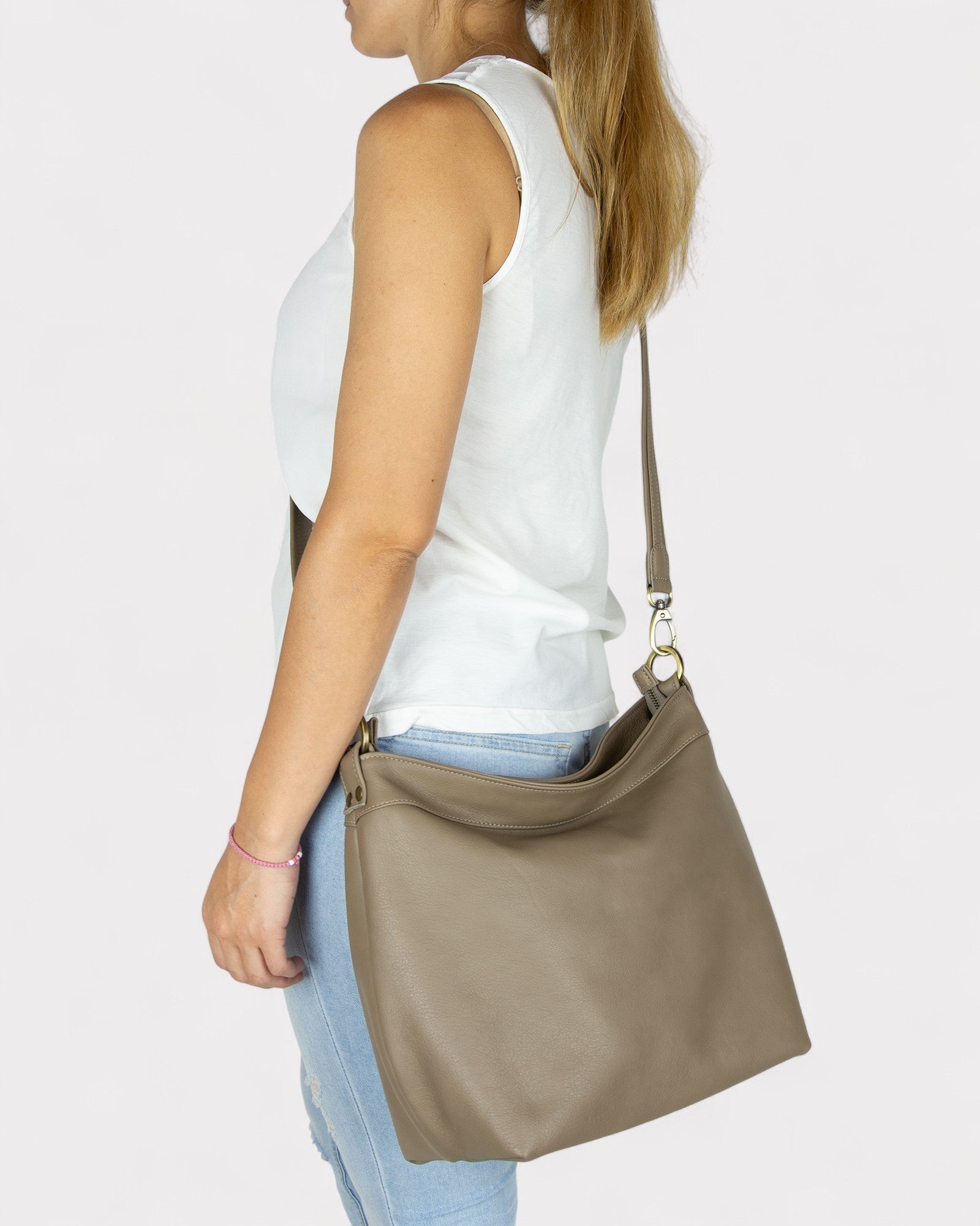 Woman carrying a taupe shoulder bag on a plain background