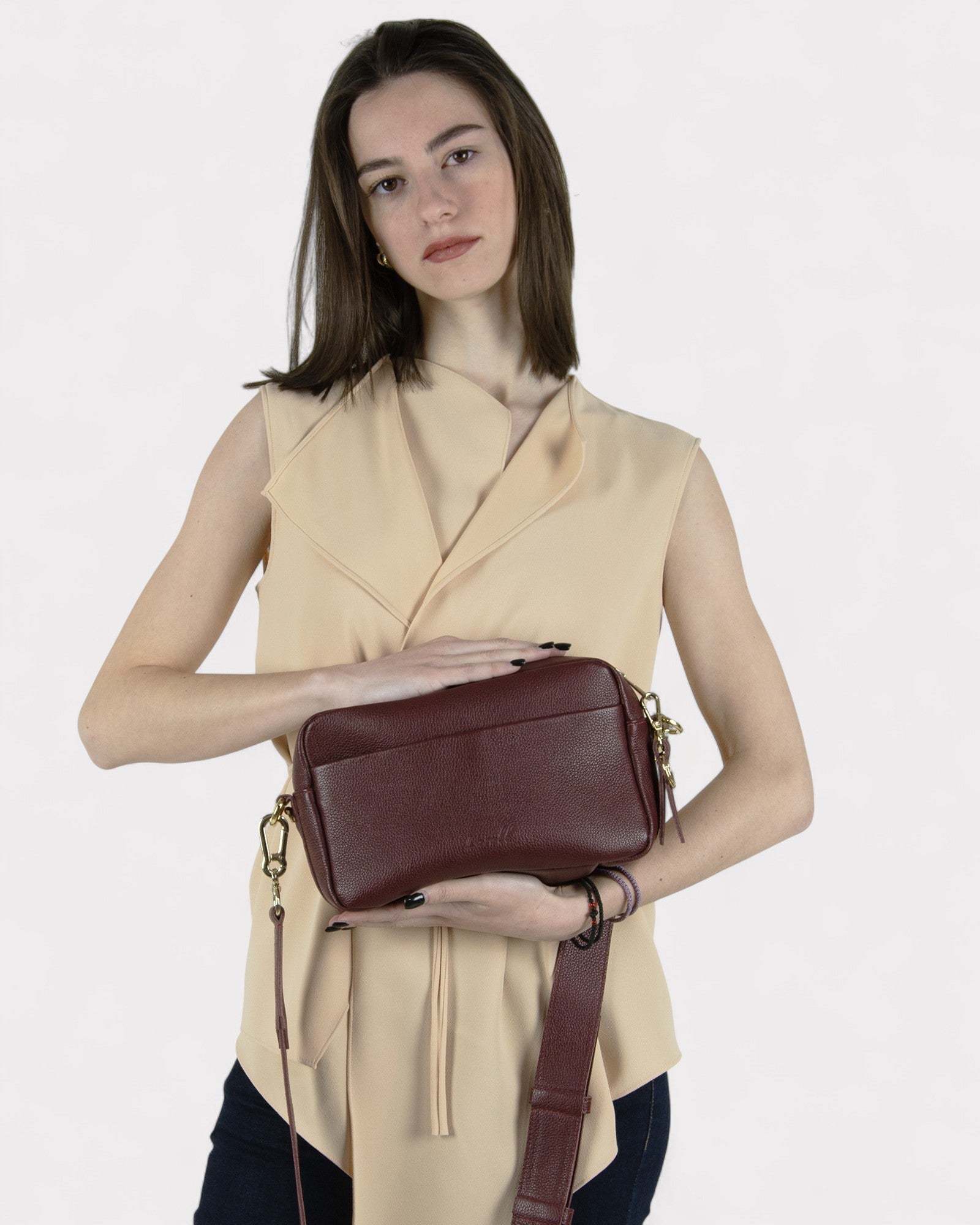 Woman holding a burgundy leather handbag against a plain background