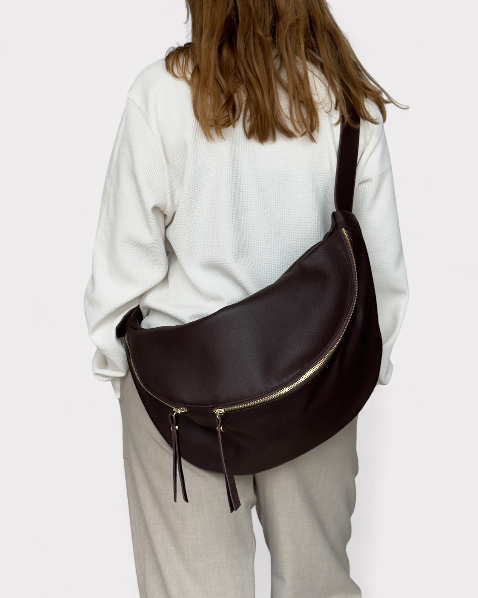 Person wearing a brown leather bag on a plain background