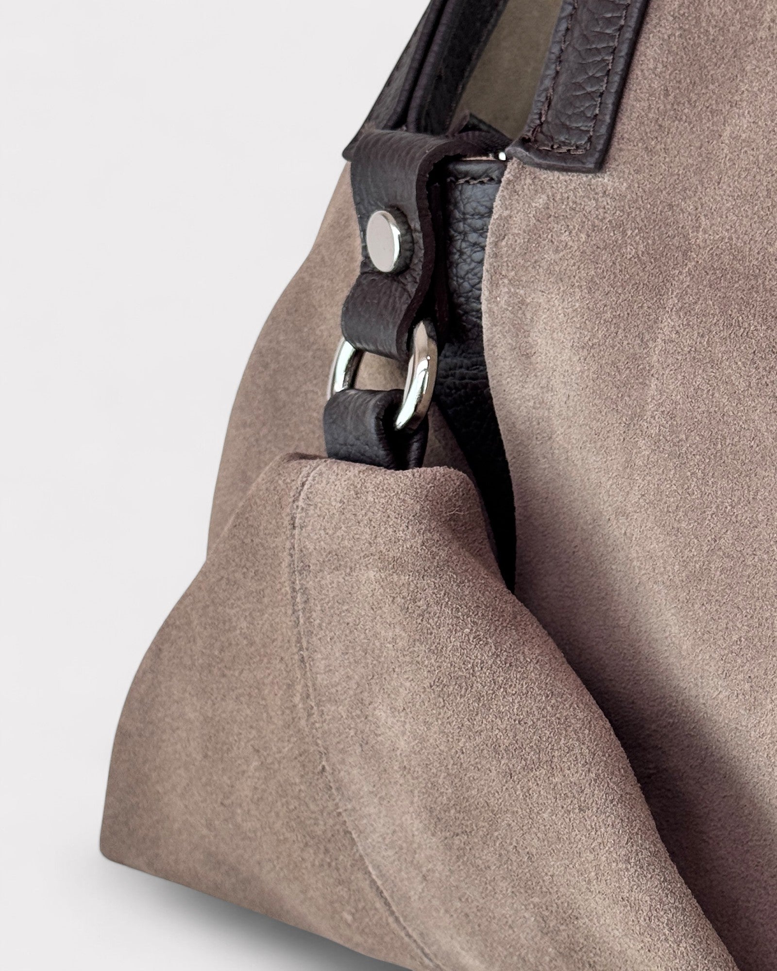 Close-up of a taupe handbag with a black strap on a light gray background