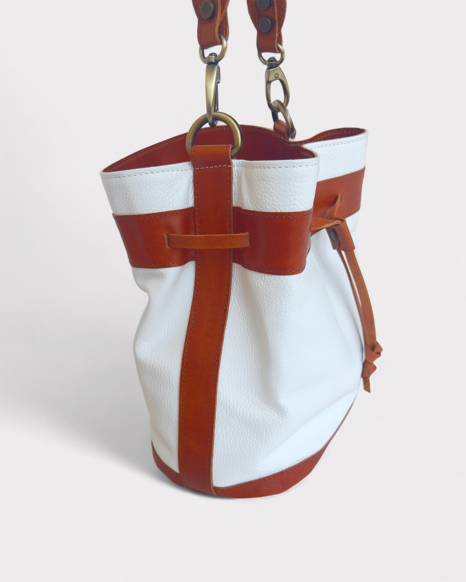 White bucket bag with brown leather straps on a light gray background