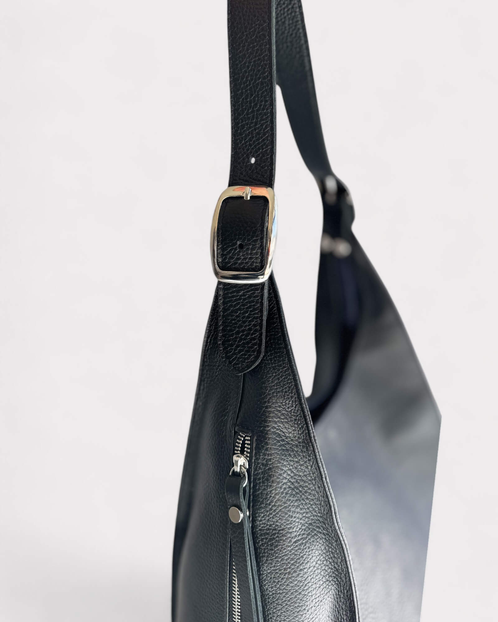 Black leather handbag with a strap and zipper detail on a light gray background