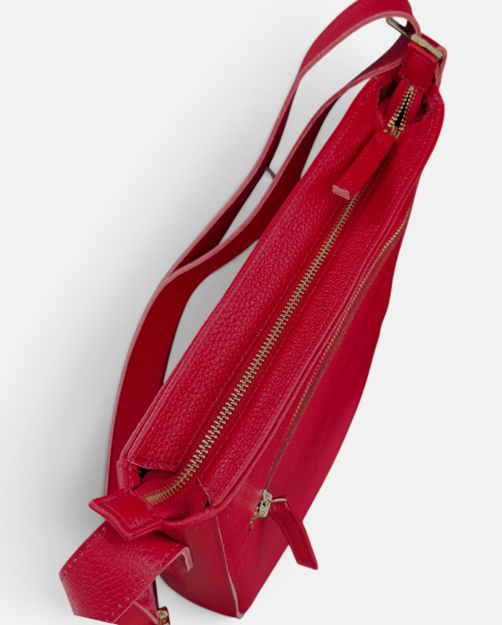 A red pebbled leather crossbody bag with gold-tone zippers and hardware, shown from an angled top-down view on a light gray background.