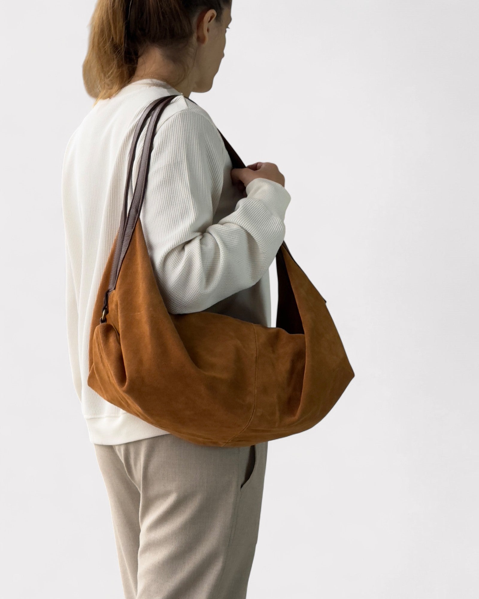 Person carrying a tan leather bag on a plain background