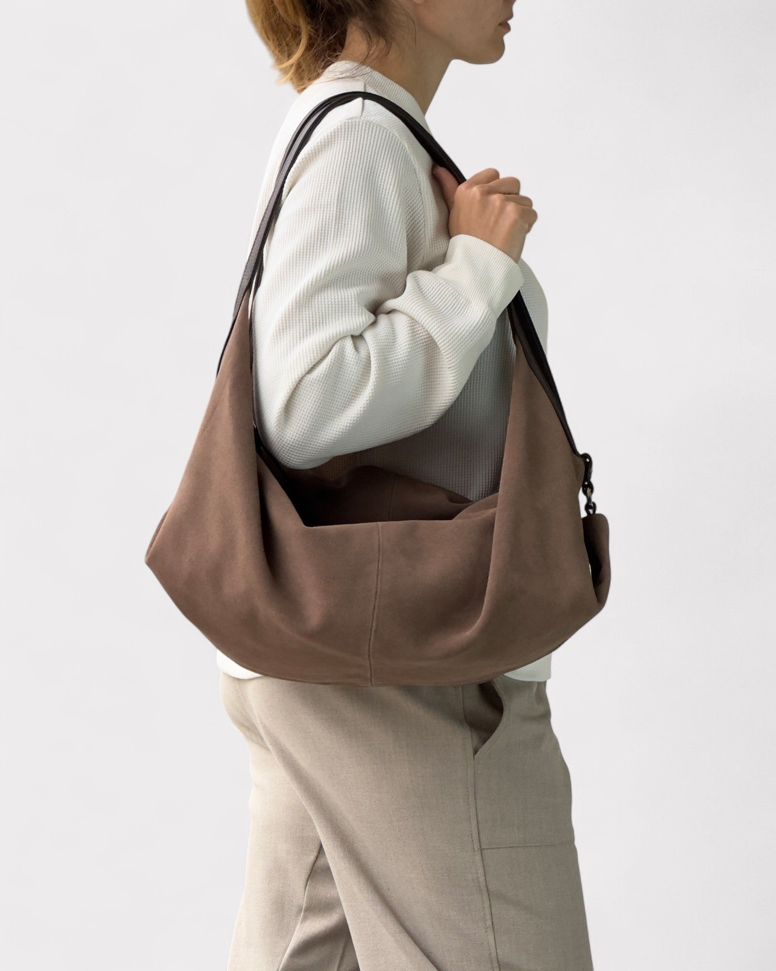 Person wearing a taupe leather bag on a plain background