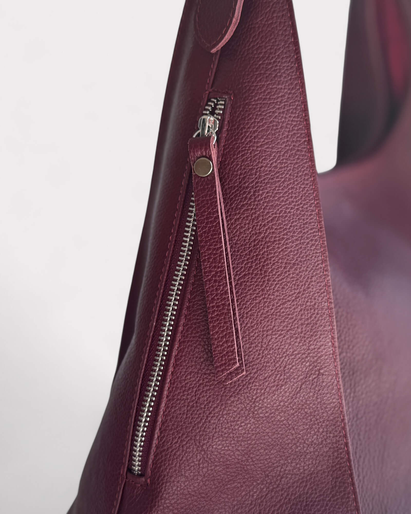 Close-up of a maroon leather handbag with a zipper on a light gray background