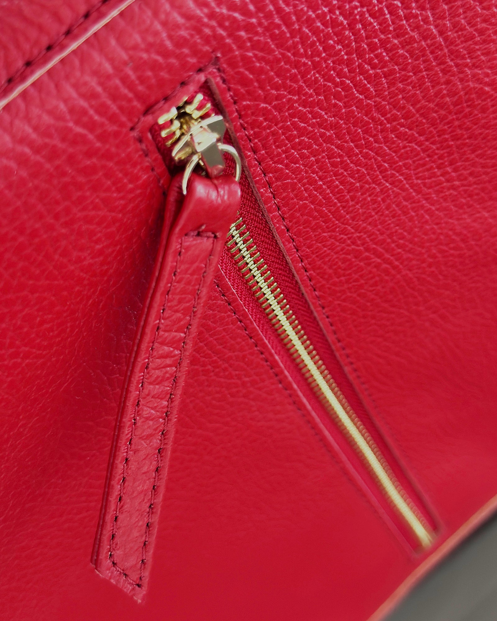 Close-up of a bright red pebbled leather bag with a gold-tone zipper and pull tab.